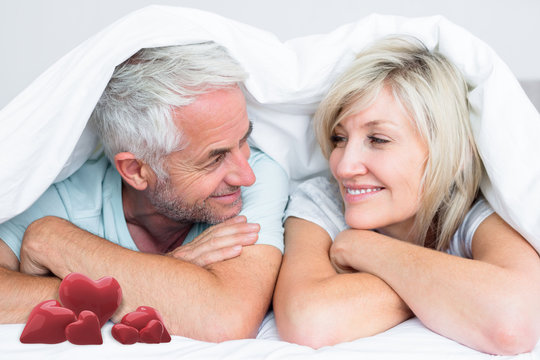 Closeup of a mature couple lying in bed against love hearts