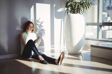 Beautiful executive sitting on floor and using mobile phone