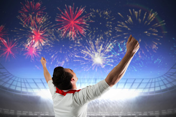 Fototapeta na wymiar Excited football fan cheering against fireworks exploding over football stadium