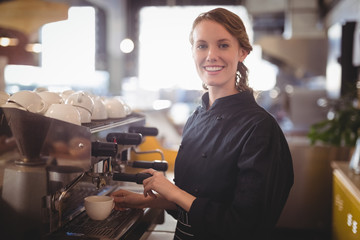 Portrait of smiling young waitress using espresso maker