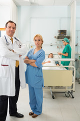 Smiling doctor and nurse standing in a hospital room while folding their arms