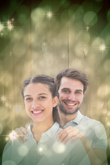 Cute couple smiling at camera against light design shimmering on green