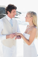 Handsome man putting ring on smiling blonde brides finger