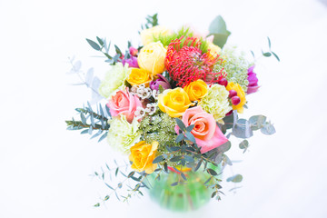 Colorful bouquet of yellow, coral and rose roses, blue eringium, red leucospermum, orange asclepia, eucalyptus and greenery
