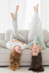 Female friends lying on sofa with legs in the air in living room