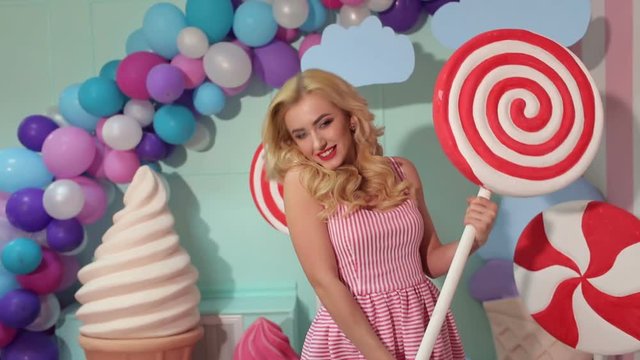 Happy girl in pink dress having fun with big plastic candy or Lollipop in the Studio. Barbie party. Candy girl.