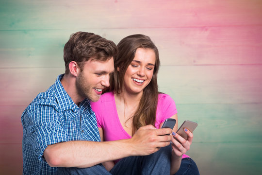 Cheerful couple with mobile phones against pink and green planks