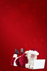 Santa lies in front of his laptop against red background