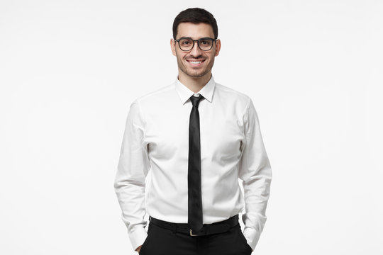 Indoor portrait of handsome European businessman pictured isolated on white background dressed in white formal shirt and black tie standing in front of camera, feeling positive, confident and calm