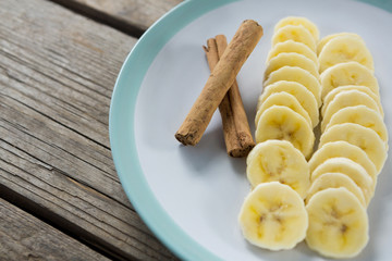 Slices of banana with cinnamon stick in plate on wooden table