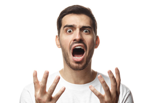 Indoor picture of young Caucasian guy pictured isolated on white background shouting with open mouth and palms spread in gesture of despair, weakness, not knowing what to do to cope with trouble