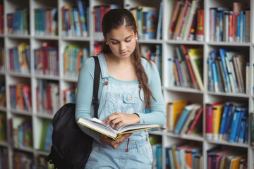 Attentive schoolgirl reading book in library