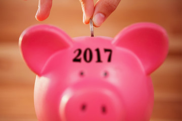 Digital image of new year 2017 against close-up of hand inserting coin in piggy bank - Powered by Adobe