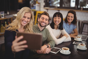 Young woman taking selfie with friends from tablet at cafe