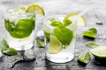 Two mojito cocktails with lime and mint in glass on a dark stone background. Closeup photo.