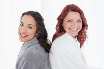 Female friends in bathrobes standing back-to-back