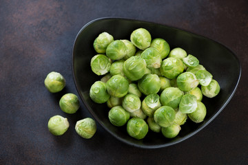 Black bowl with fresh uncooked brussels sprouts over dark brown metal background, horizontal shot, elevated view