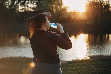 Overweight woman drinking water after jogging