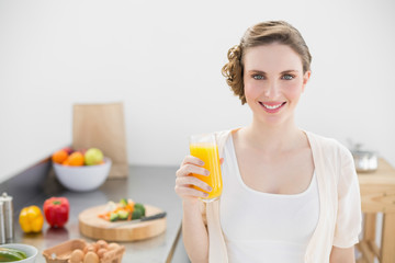 Obraz na płótnie Canvas Beautiful woman posing in her kitchen holding a glass of orange juice