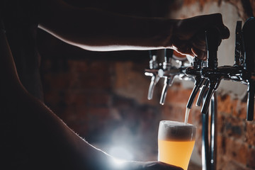 Close-up of barman pours light cold filtered beer in glass beaker.