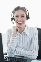 Laughing chic agent wearing headset sitting at her desk