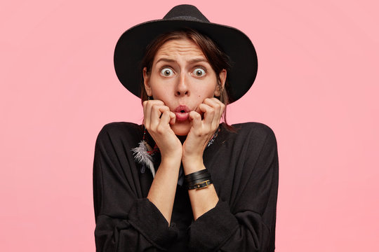 Frightened Caucasian female wears cowboy style clothes, looks with puzzled and scared expressioon, has eyes popped out, isolated over pink background. People, amazement and emotions concept.