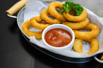 Delicious onion rings with tomato sauce serve on metal bowl for food background or texture.