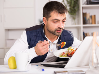 Positive young male holding  fork, eating vegetable salad