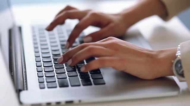 Business girl with beautiful hands typing on keyboard, running on laptop. Writes the text, communicates in messengers and edits articles. A beautiful light and bokeh on the hands of.