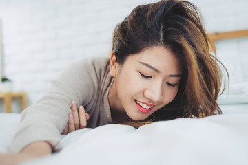 Portrait beautiful young Asian woman on bed at home in the morning. Cheerful Asian woman wearing a comfortable sweater and smiling on her bed. Relaxing room. lifestyle asia woman at home concept.