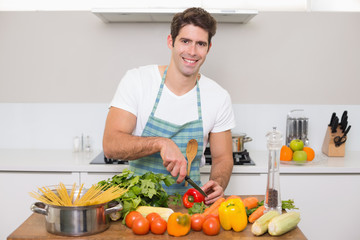 Fototapeta premium Smiling young man chopping vegetables in kitchen