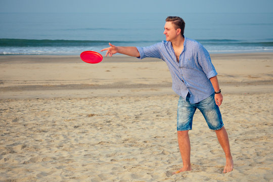 young man playing flying disk on the beach in the morning