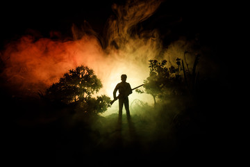 Man with riffle at spooky forest at night. Strange silhouette of hunter in a dark spooky forest at...