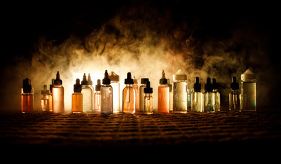 Vape concept. Smoke clouds and vape liquid bottles on dark background. Light effects. Useful as...
