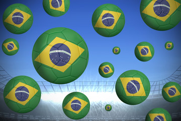 Footballs in brasil flag colours against large football stadium under bright blue sky