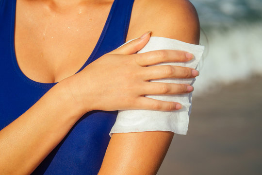 young woman rubs a wet napkin on the skin of hands on the beach