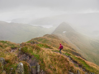 Fototapeta na wymiar A hiker walking down Long Stile Ridge towards Haweswater Reservior on a cold overcast day in the English Lake District, UK.