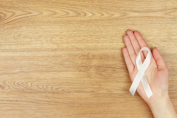 Oncological disease concept. Woman's hand with a white ribbon as a symbol of lung cancer isolated...