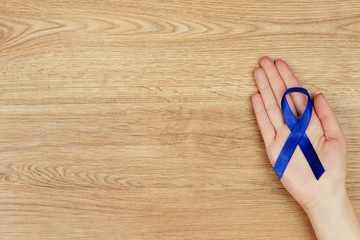Oncological disease concept. Woman's hand with a blue ribbon as a symbol of bowel cancer isolated...