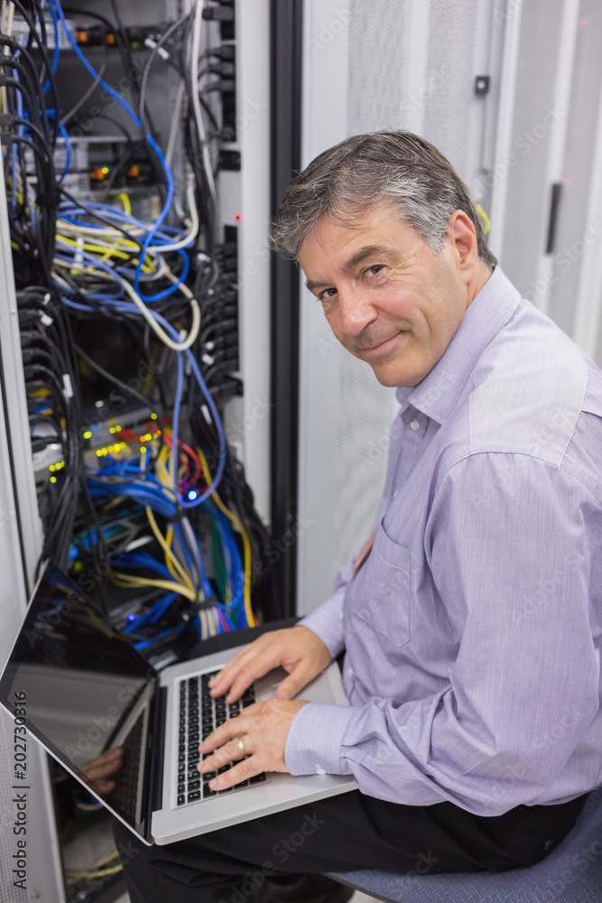 Poster Man typing on laptop while doing server maintenance