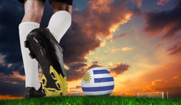 Composite image of football boot kicking uruguay ball against green grass under dark blue and orange sky