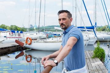 Yachtsman near standing near of pier barrier with boats. Bearded man looking to far before journey near of yacht. Travel tourism vacation and people concept.