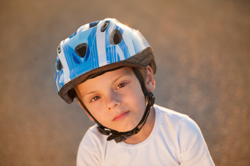 portrait or cute small child in sport helmet standing on abandoned road in warm summer sunset