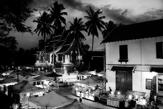 Famous night market in Luang Prabang, Laos with illuminated temple. Black and white