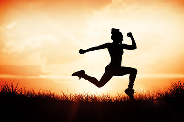 Fit brunette running and jumping against orange sunrise