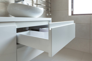 Opened U-shaped drawer in a bathroom furniture, white glossy front, handless design. 