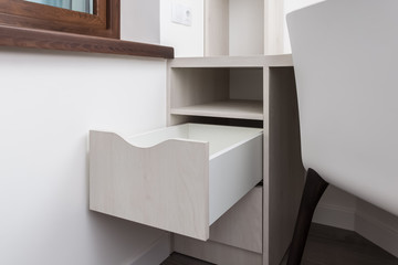 Opened drawer in a cabinet under a desk. Wooden beige front of the drawer. 