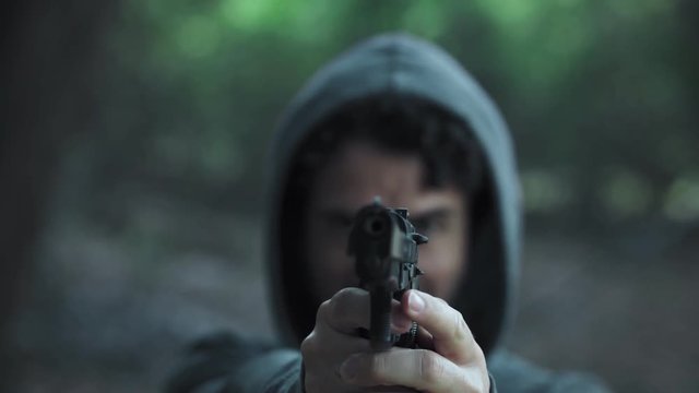 hooded young man pointing the gun at camera