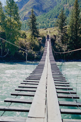 Obraz premium Young man walks along a suspension bridge across a mountain river Katun in the early autumn