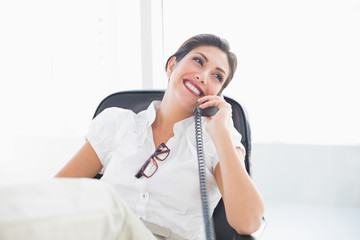 Reclining businesswoman sitting at her desk talking on phone